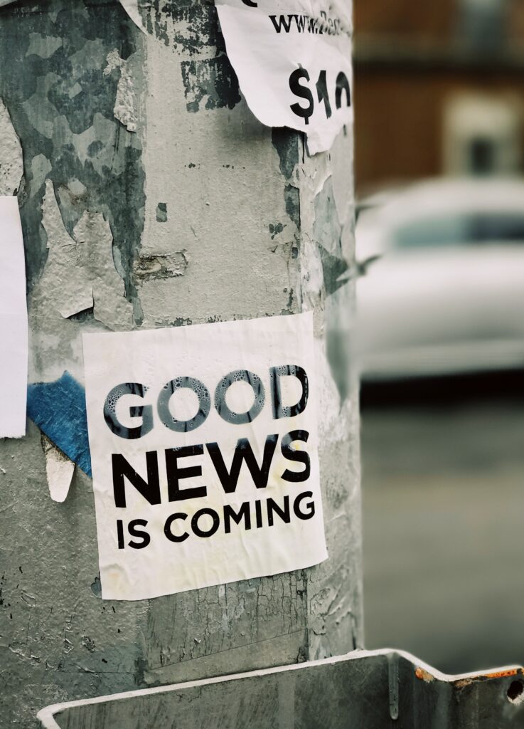 Photo of a sign posted to a tree stating "good news is coming"