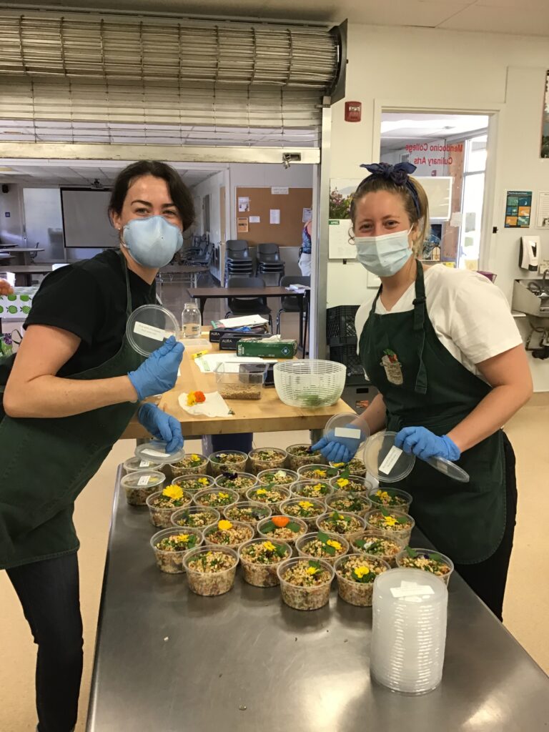 two volunteers prepare local food in kitchen wearing face masks