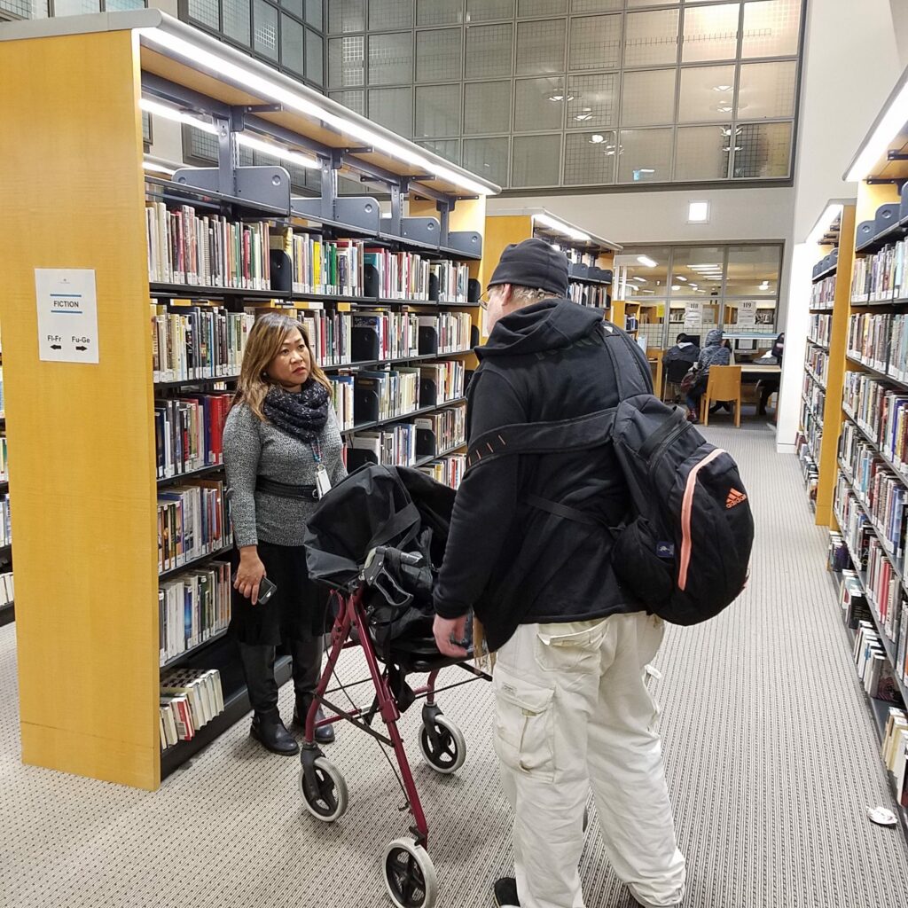Photo of librarian speaking with a houseles individual in front of library book shelves
