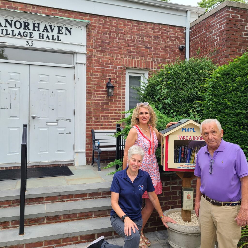Photo of two women and one man standing in front of a little free library 