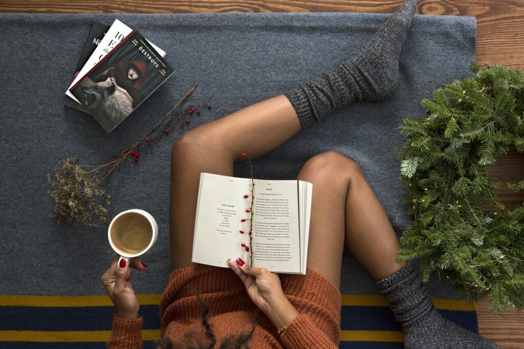 Woman sits reading books wearing cozy socks and with a cup of coffee in hand