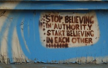 graffiti on a wall saying: "Stop believing in authority, start believing in each other."