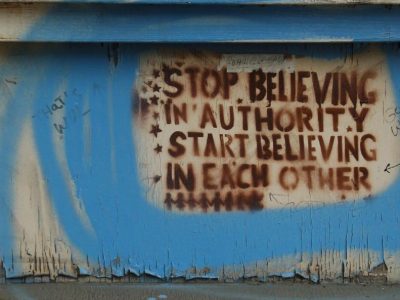 graffiti on a wall saying: "Stop believing in authority, start believing in each other."